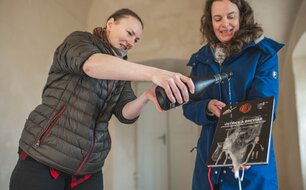 Tereza Sýkora Řeháková křtí knihu Ústřice a breviář, již přidržuje Marcela Waldmannová, vedoucí výzkumu jímky a iniciátorka tohoto publikačního počinu, nad samotnou jímkou. Foto T. Chlup, 2024.